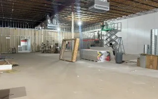 Interior build-out showing drywall installation, scaffolding, and ductwork during Omega Contracting retail project