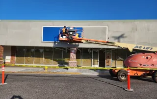 Exterior construction work with crew installing new storefront signage using a lift at retail renovation site