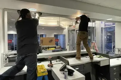 Workers installing new bullet resistant glass panels at the teller line for an International Banking Company renovation project.